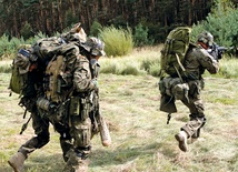 Oddział wychodzi z lasu. Żołnierze idą spokojnie z ciężkimi plecakami, z bronią gotową do strzału.