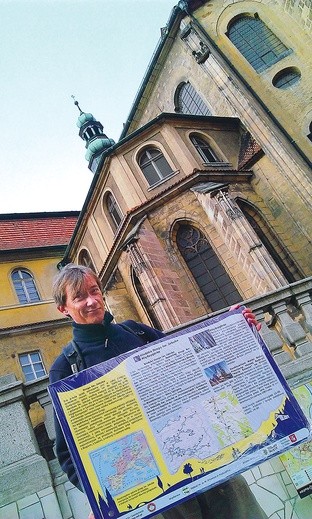  Emil Mendyk pokazuje tablicę informacyjną, która stanie na początku szlaku w Międzygórzu obok oddziału PTTK. Z tyłu kłodzka bazylika Wniebowzięcia NMP, w której znajduje się kaplica św. Jakuba