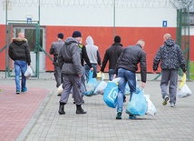 Więźniowie w asyście strażników odbierają paczki od najbliższych