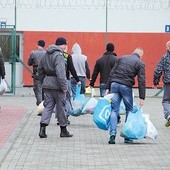 Więźniowie w asyście strażników odbierają paczki od najbliższych