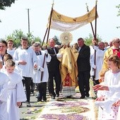 Kapłan z Najświętszym Sakramentem kroczy  po kwietnym kobiercu.