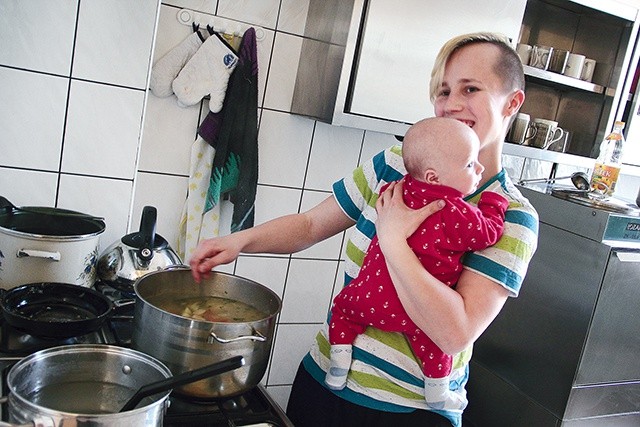 Dyżurująca w kuchni mama gotuje z synkiem na ramieniu. Trudne? Owszem, ale we własnym domu robiłaby dokładnie to samo.         