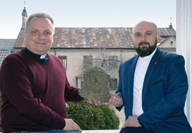 Ks. Robert Kowalski (z lewej) i ks. Damian Drabikowski pokazują znaleziony podczas remontu stary żeliwny odlew głowy Chrystusa. W tle dawna kaplica, obecnie magazyn radomskiej organizacji.