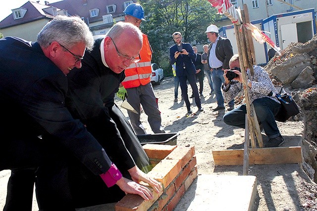 Biskup Marian Niemiec i o. Piotr Świerczok wspólnie wmurowują symboliczną cegłę.