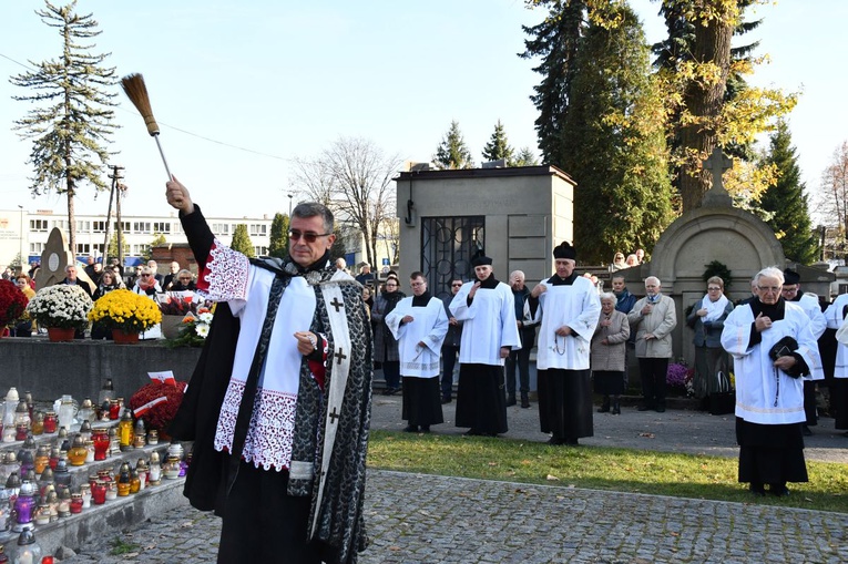 Ks. Jerzy Jurkiewicz kropi wodą święconą groby podczas procesji we Wszystkich Świętych.
