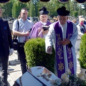 Ks. Bogusław Wermiński posypujący ziemią trumnę zmarłego szafarza.