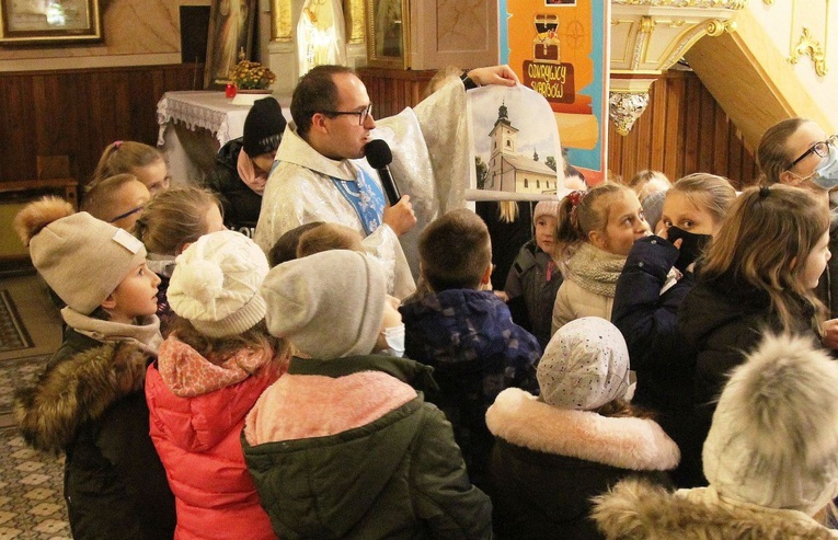 Ks. Marcin Samek prezentuje dzieciom zdjęcie kościoła św. Jakuba w Rzykach, znalezione w skrzyni tajemnic.