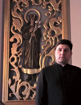 ▲	Ks. Rafał Piekarski przy płaskorzeźbie świętego w kaplicy radomskiego seminarium.