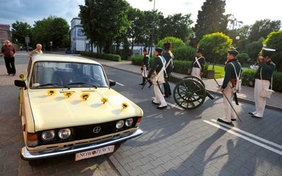Polscy artylerzyści w mundurach sprzed 180 lat mijają samochód nowożeńców pod klasztorem bernardynów