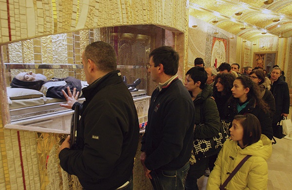 Pielrzymi modląc się, dotykają szyby osłaniającej ciało świętego 