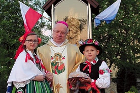  Bp Józef Zawitkowski wraz z dziećmi ubranymi w stroje łowickie przy maryjnej kapliczce