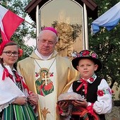  Bp Józef Zawitkowski wraz z dziećmi ubranymi w stroje łowickie przy maryjnej kapliczce