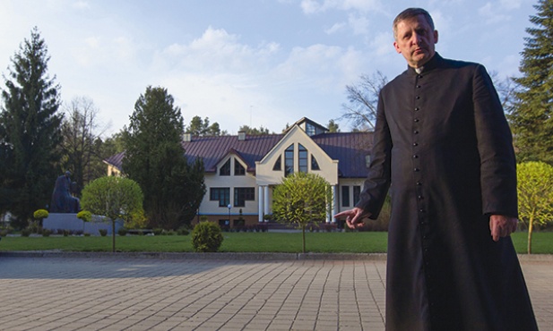 Ks. rektor Piotr Brzeski na tle jednego z budynków seminarium w Brzuchowicach; po lewej pomnik Jana Pawła II