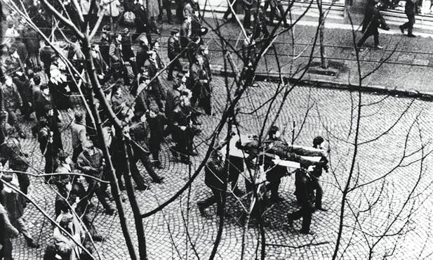 Gdynia, 17 grudnia 1970. Ulicą Świętojańską w kierunku centrum przechodzi pochód, demonstranci niosą na drzwiach zwłoki Zbigniewa Godlewskiego, który zginął w okolicy przystanku Gdynia -Stocznia, przeszyty serią z karabinu maszynowego