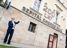  Dyrektor szpitala Joanna Niestrój-Ostrowska pokazuje neon na frontowej ścianie budynku zapraszający na obchody 200-lecia istnienia