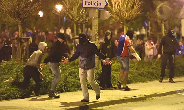 3.05.2015. Knurów. Polska. Pseudokibice rzucają niebezpiecznymi przedmiotami w kierunku policji ochraniającej komisariat. W sobotę 2 maja podczas meczu piłki nożnej między Concordią i Ruchem Radzionków doszło do zamieszek, w trakcie których jeden z kibiców został postrzelony przez policjanta z broni gładkolufowej. Ranny zmarł w szpitalu. W nocy z 2 na 3 maja doszło do starć pseudokibiców z policją przed szpitalem i komisariatem policji w Knurowie. 