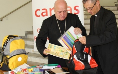 Bp Piotr Greger pakuje do plecaka Caritas zakupioną przez siebie szkolną wyprawkę