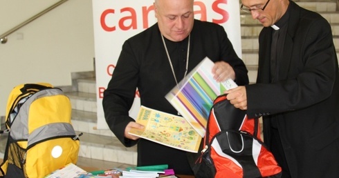 Bp Piotr Greger pakuje do plecaka Caritas zakupioną przez siebie szkolną wyprawkę