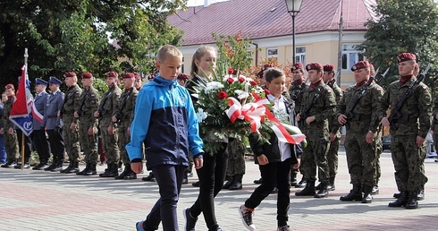 Delegacja uczniów niesie wiązankę kwiatów pod pomnik na pl. Kościuszki