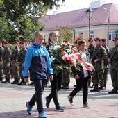 Delegacja uczniów niesie wiązankę kwiatów pod pomnik na pl. Kościuszki