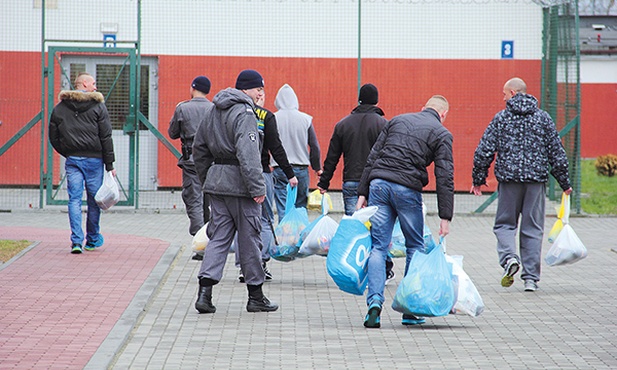 Więźniowie w asyście strażników odbierają paczki od najbliższych