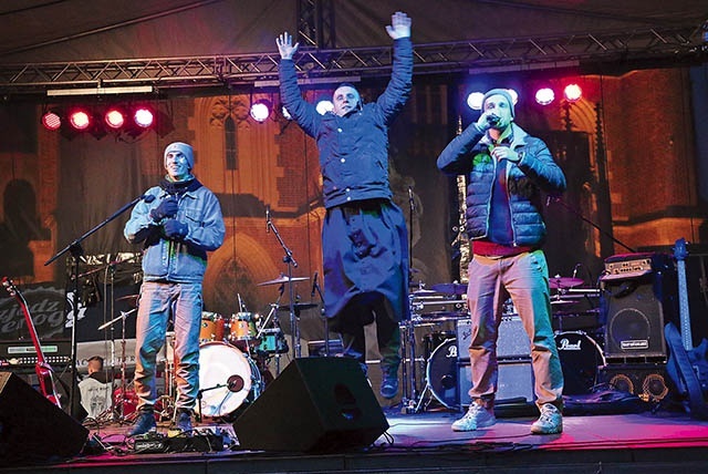  Na scenie podczas występu młodzi raperzy Kocik i Malej, a w środku  ks. Jakub Bartczak pokazuje młodzieży, jak należy się bawić na koncertach