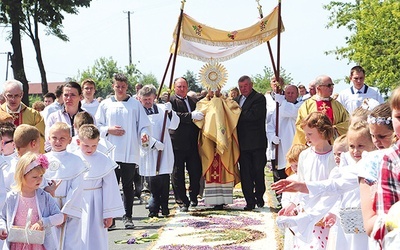 Kapłan z Najświętszym Sakramentem kroczy  po kwietnym kobiercu.