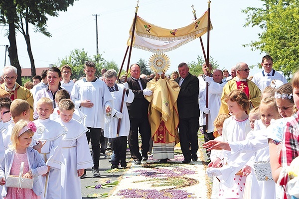 Kapłan z Najświętszym Sakramentem kroczy  po kwietnym kobiercu.