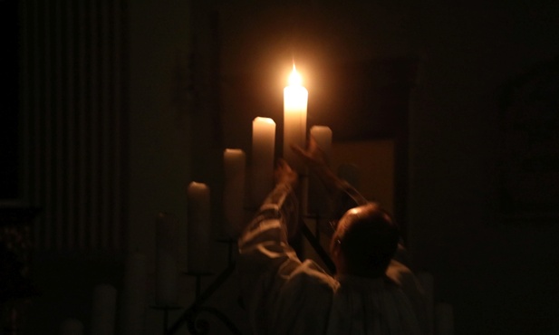 Ks. Marcin Wróbel ponownie ustawia płonącą świecę na świeczniku...
