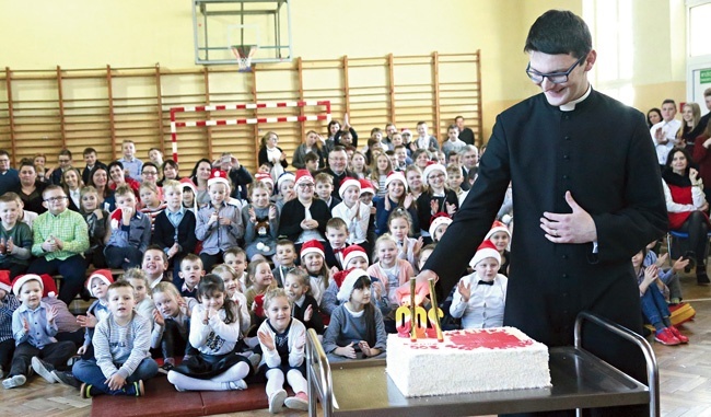 Ksiądz Damian Warzecha zapala świeczki  na jubileuszowym torcie.