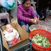 Ciepło ubrane dziecko w kartonie obok babci krojącej brokuły.
11.12.2017 Tajpej, Tajwan