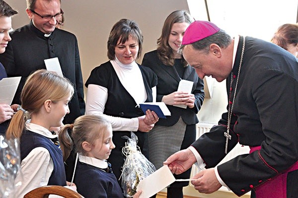 ▲	Biskup Jeż dzieli się opłatkiem z dziećmi ze szkoły katolickiej.