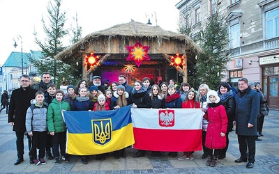 ▲	Pamiątkowe zdjęcie uczestników kolędowania przy szopce ustawionej przed ratuszem.