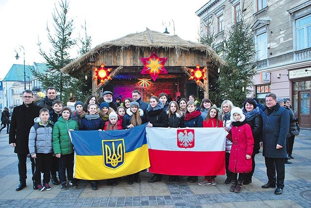 ▲	Pamiątkowe zdjęcie uczestników kolędowania przy szopce ustawionej przed ratuszem.