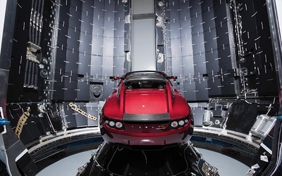 Ten sportowy samochód Tesla Roadster w kolorze wiśniowym leci w kierunku Marsa  na pokładzie rakiety Falcon Heavy.