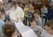 Ks. Tomasz Orłowski odwija zwój Listu do Rzymian, spisany przez dzieci i młodzież radomskiej katedry