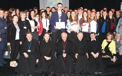 ▲	Siedzą od lewej: ks. Marcin Rogala, ks. Jacek Kucharski, bp Adam Odzimek, ks. Stanisław Łabendowicz i ks. Mirosław Prasek, filipin. Na środku stoi Tomasz Sar, a obok z dyplomami Emila Myrta i Martyna Sowa (z prawej).