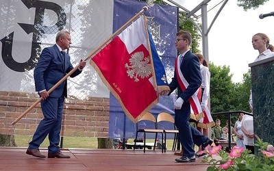 Poświęcony sztandar przekazuje uczniom Jan Słuszniak, dyrektor placówki.