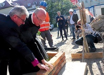 Biskup Marian Niemiec i o. Piotr Świerczok wspólnie wmurowują symboliczną cegłę.