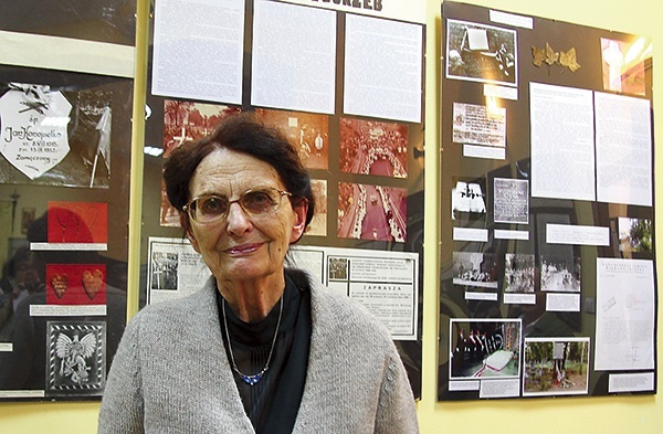 ◄	Danuta Skraba na tle ekspozycji „Zmarli zobowiązują żyjących”.