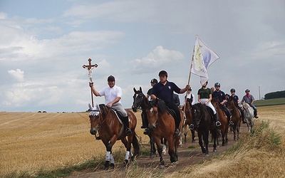 ▲	Na czele pielgrzymki jadą jeźdźcy z krzyżem i chorągwią stowarzyszenia. 