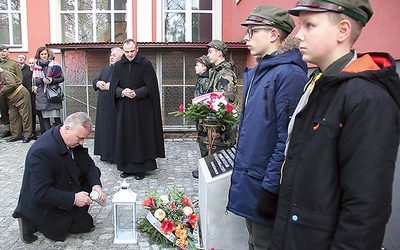 Jan Kondek zapala znicz przed odrestaurowaną płytą pamiątkową.