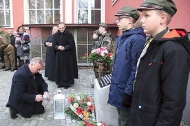 Jan Kondek zapala znicz przed odrestaurowaną płytą pamiątkową.