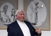 Ks. Stanisław Drąg na tle swych rysunków, które przedstawiają Jana Pawła II.