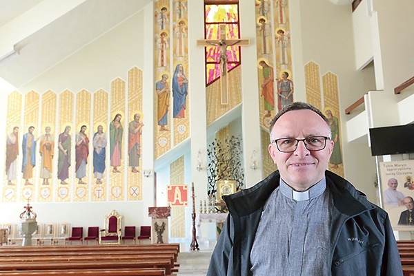 Ksiądz Emil Myszkowski na tle polichromii ściany ołtarzowej.