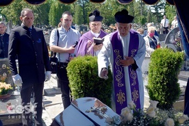 Ks. Bogusław Wermiński posypujący ziemią trumnę zmarłego szafarza.