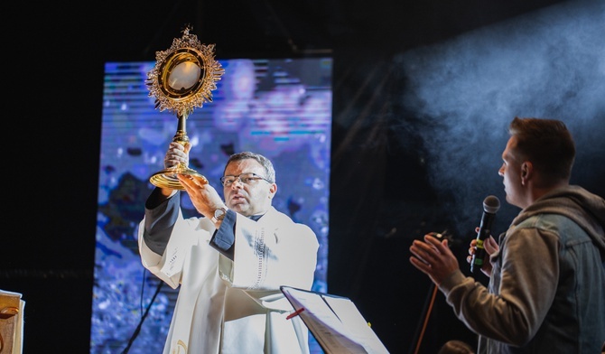 Ks. Krzysztof Iwaniszyn wnosi na scenę monstrancję z Najświętszym Sakramentem.