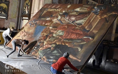 Konserwatorzy podnoszący wielkoformatowy obraz w katedrze.
