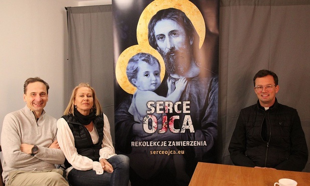 Od lewej: Marek i Adriana Zarembowie oraz ks. Mateusz Dudkiewicz przy rekolekcyjnym banerze, zapraszjącym na 27 dni z Sercem Ojca.