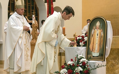 Proboszcz ks. Jacek Orszulak składa relikwiarz obok obrazu papieża Polaka.